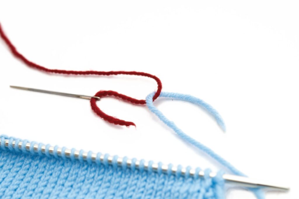 Blaues Strickprojekt mit rotem Garn. Handgemacht, DIY, feine Musterstrickarbeit.