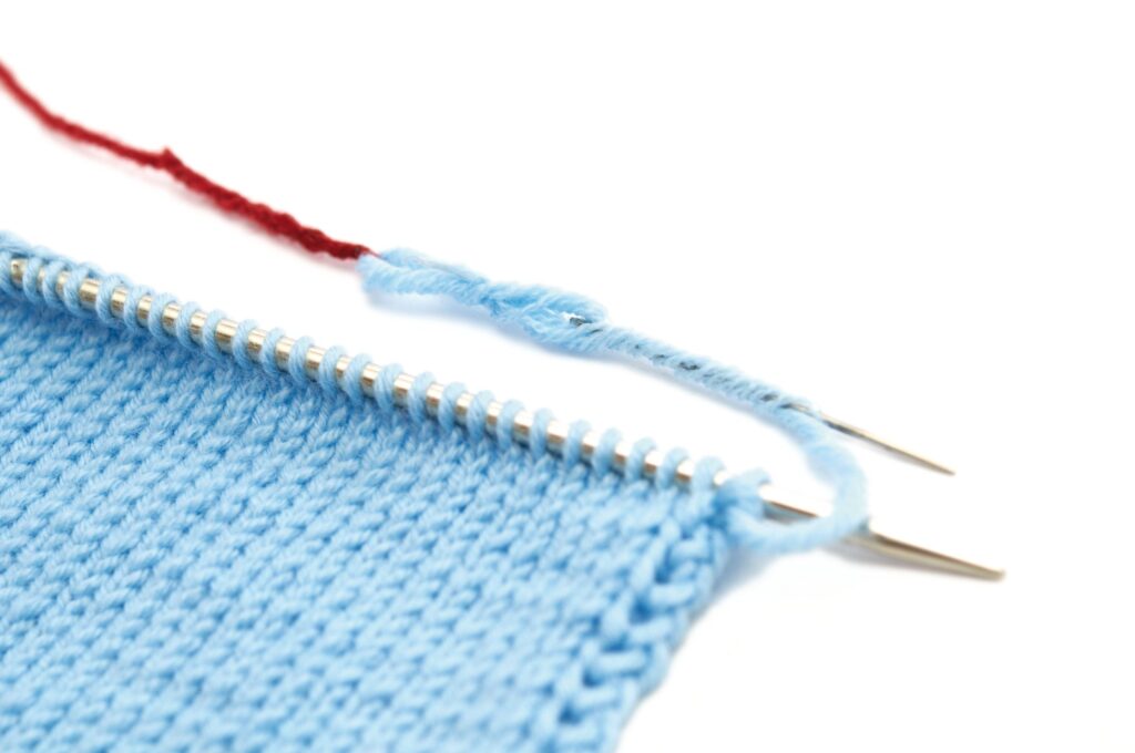 Hellblaues Strickstück, feine Musterung, präsentiert auf Nadeln. DIY, handgemacht, eleganter Look.