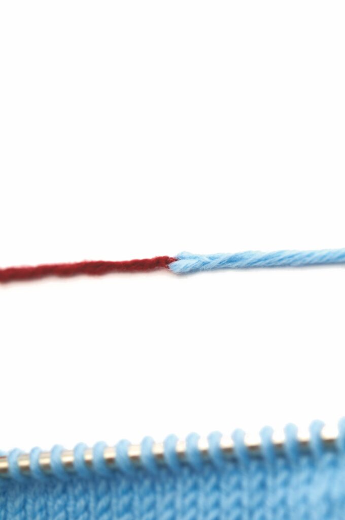 Handarbeit mit blauem Garn und rotem Akzent, DIY-Charme, gleichmäßige Maschen auf Stricknadel.