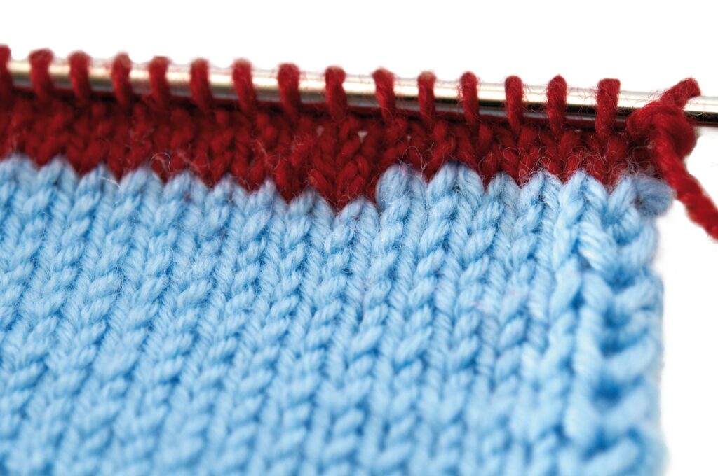 Modisch gestricktes Stück, hellblau mit oberer weinroter Borte. Handarbeit und selbstgemacht.