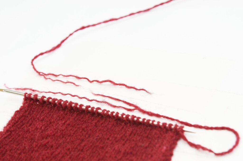 Tiefrote, handgearbeitete Maschen auf Nadeln. Weiches, modisches Strickmuster. DIY-Trend.