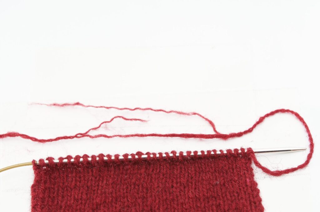 Rotes Strickstück auf Nadel, gleichmäßiges Muster. Modisch, DIY, handgemacht, warm und einladend.