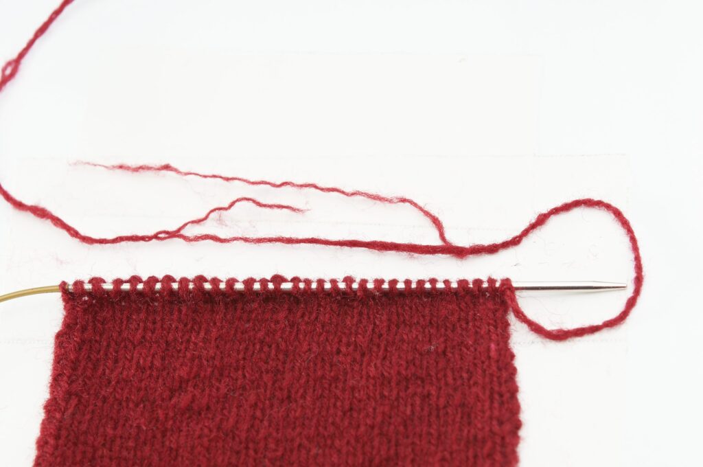 Handgefertigtes Strickstück in intensivem Rot. Gleichmäßiges Maschenmuster, DIY-Charme.