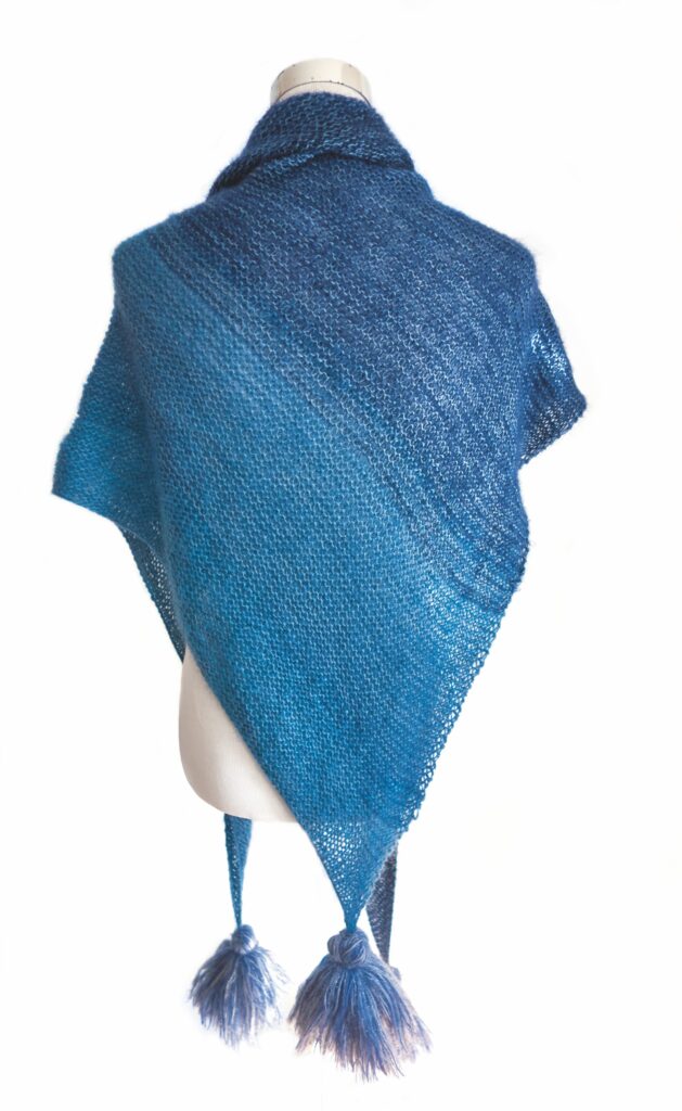 Modischer, handgemachter Schal in Blauverlauf, texturiertes Muster, dreieckiger Schnitt, Pompons als Detail.