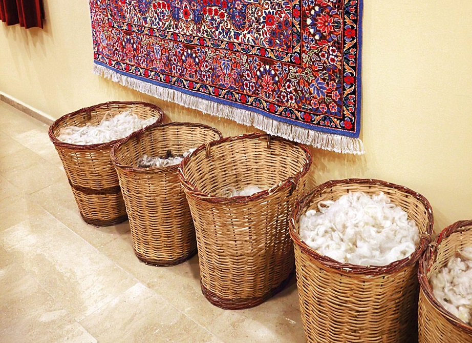 Farbiger, gemusterter Teppich mit handgewebten Details. Körbe gefüllt mit weißer Wolle, rustikale Handarbeit.